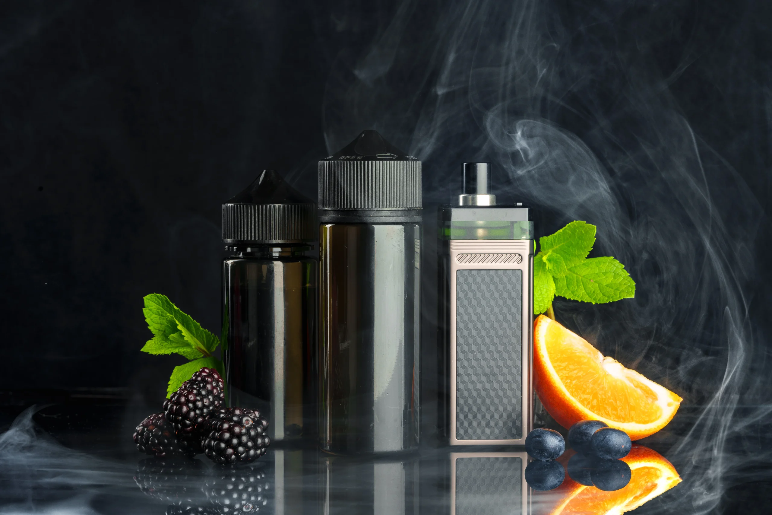 Three vape juice bottles and a vape device are surrounded by fresh blackberries, blueberries, an orange slice, and mint leaves, with swirling vapor against a dark background—perfect for those seeking cannabis delivery NYC & Long Island, NY.