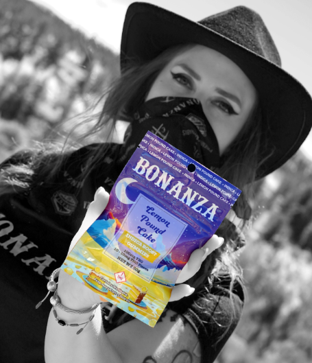 A woman wearing a black hat and bandana holds a colorful package of “Bonanza Lemon Pound Cake” cannabis edibles. The image is mostly black and white except for the vividly colored product.
