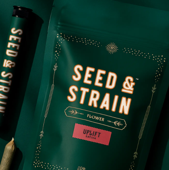 A dark green package labeled "Seed & Strain Flower" with the word "Uplift Sativa" in a pink box, next to a matching branded tube and a rolled joint.
