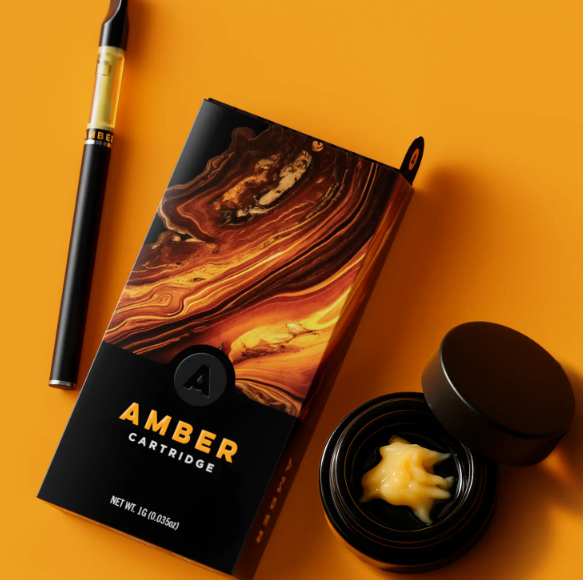 A vape pen, a black and amber swirl cartridge box labeled "Amber Cartridge," and a small open container with a creamy yellow substance are displayed on an orange surface.