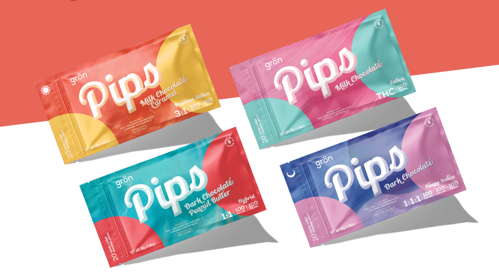 Four colorful rectangular Grön Pips chocolate bar packages are displayed diagonally on a red and white background. Each package features a distinct color and flavor, including milk and dark chocolate varieties.