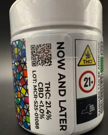 A white cannabis container labeled "NOW AND LATER" displays THC 21.4%, CBD <1.0%, a QR code, and warnings for THC, age 21+, and New York State compliance, with a colorful geometric pattern on the side.