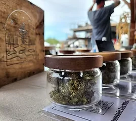 Glass jars of cannabis flower on a table beside a branded wooden box, perfect for storage or display.