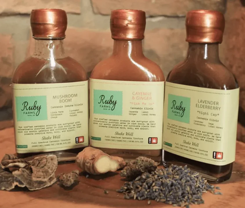 Three Ruby Farms elixirs are displayed with mushrooms, ginger, and lavender arranged in front.