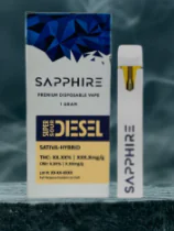 A Sapphire disposable vape and its box labeled “Super Sour Diesel” Sativa-Hybrid rest on a dark surface.