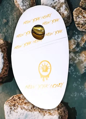 A white surfboard on rocks shows gold “NEW YORK HONEY” text and a Statue of Liberty graphic on top.